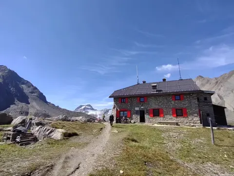 Rifugio in pietra con le imposte rosse, raggiunto da un sentiero