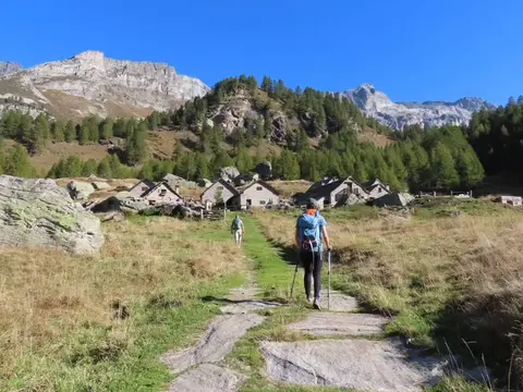 Escursionista su un sentiero lastricato verso un alpeggio di case in pietra