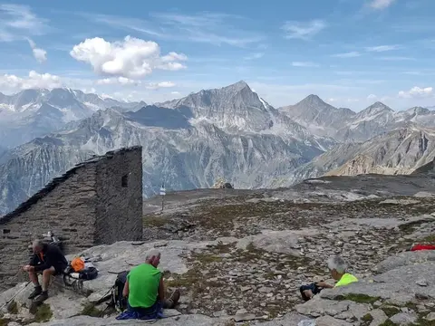 Escursionisti in sosta accanto a una baita, con le montagne sullo sfondo
