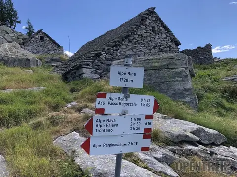 Il cartello dell'alpe Rina, 1720 m, accanto a una baita in pietra