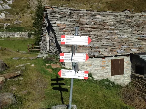 Il palo segnaletico dell'alpe Lago accanto a una baita in pietra